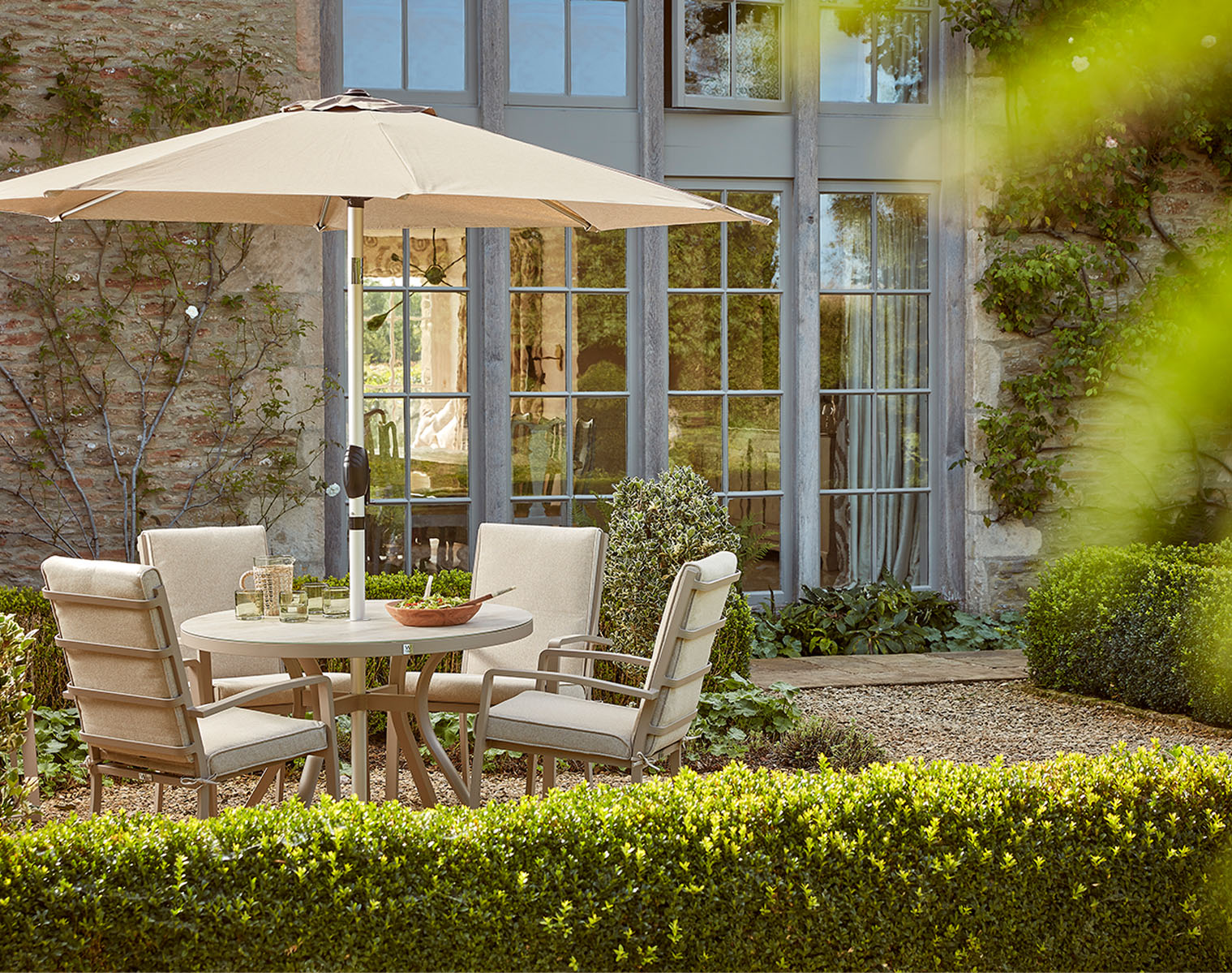 A garden dining set beneath a cream parasol outside a country house